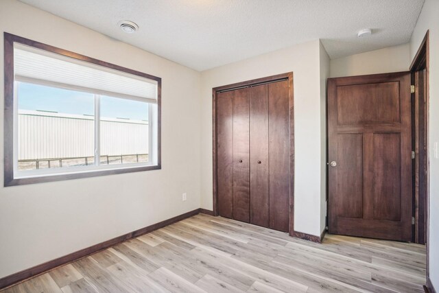 unfurnished bedroom featuring light hardwood / wood-style flooring, a textured ceiling, and a closet