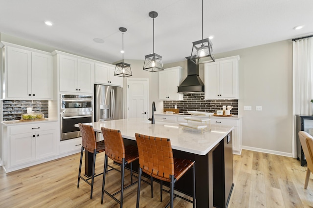 kitchen with pendant lighting, premium range hood, stainless steel appliances, an island with sink, and white cabinets