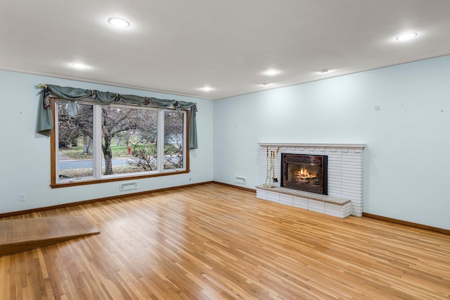 unfurnished living room featuring light wood-type flooring, a brick fireplace, and crown molding