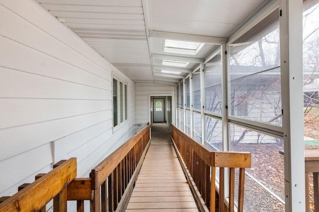 corridor with wooden walls, hardwood / wood-style floors, a healthy amount of sunlight, and lofted ceiling with skylight