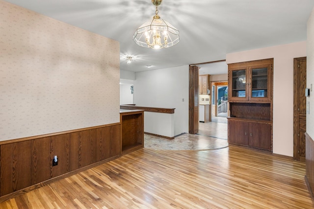 unfurnished room with light wood-type flooring, wooden walls, and a notable chandelier