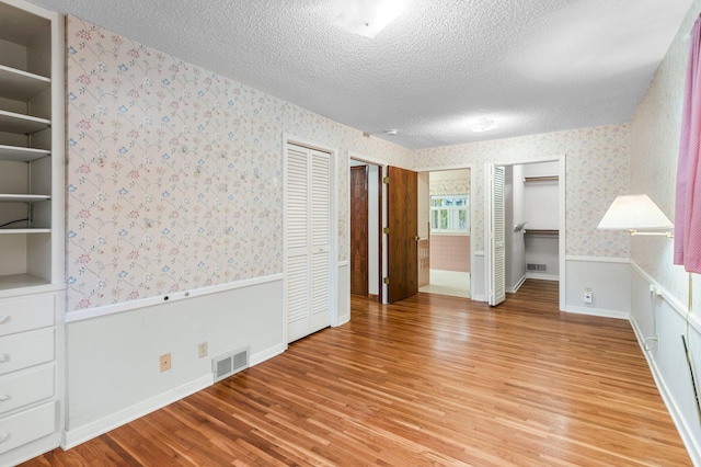 unfurnished bedroom with hardwood / wood-style flooring, a textured ceiling, and two closets