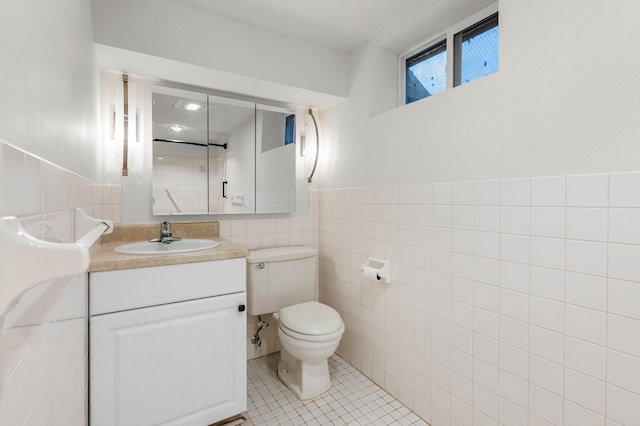 bathroom featuring tile patterned floors, vanity, toilet, and tile walls