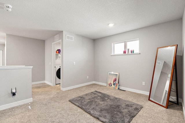 interior space featuring washer / dryer, light colored carpet, and a textured ceiling