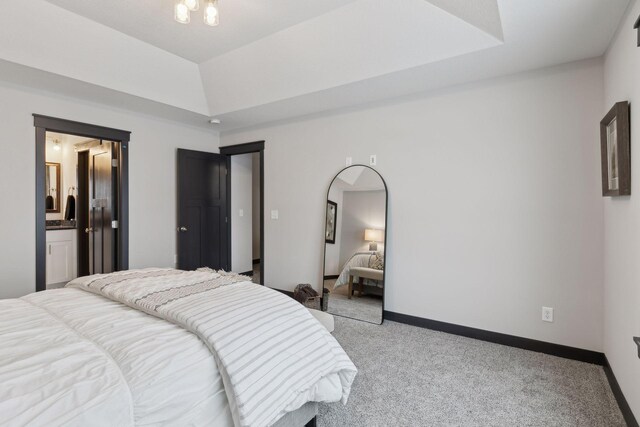 bedroom featuring ensuite bathroom, a raised ceiling, and light colored carpet