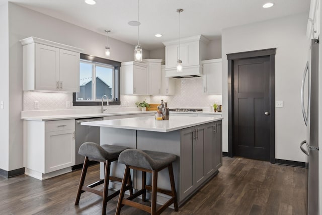 kitchen with appliances with stainless steel finishes, white cabinets, dark hardwood / wood-style floors, a kitchen island, and hanging light fixtures