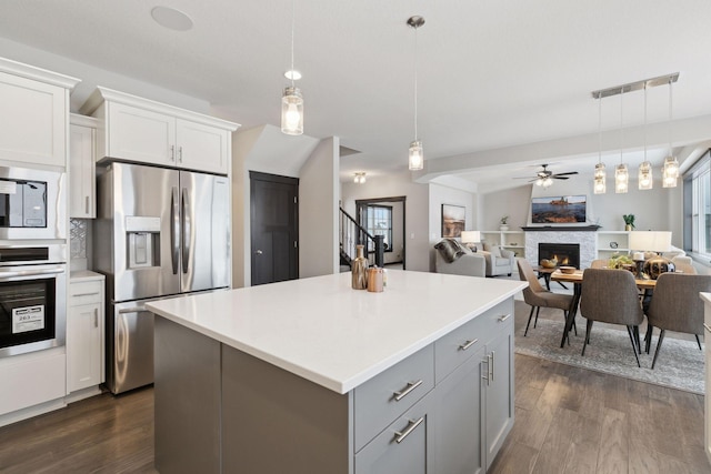 kitchen with pendant lighting, white cabinets, ceiling fan, a fireplace, and stainless steel appliances