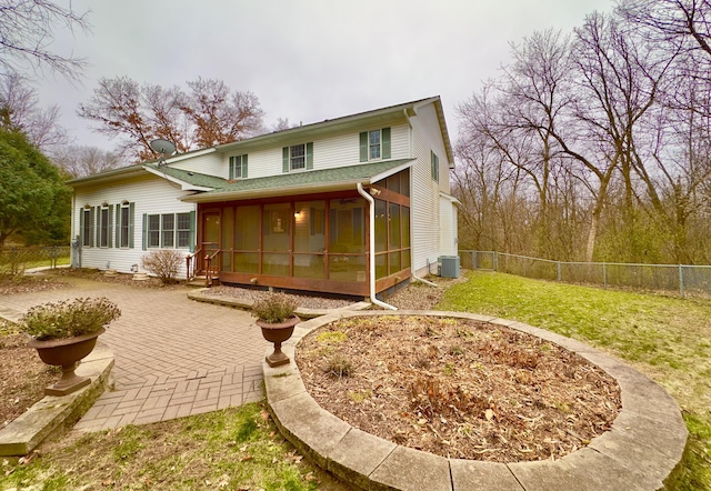 back of property with a sunroom, a patio, a lawn, and central AC