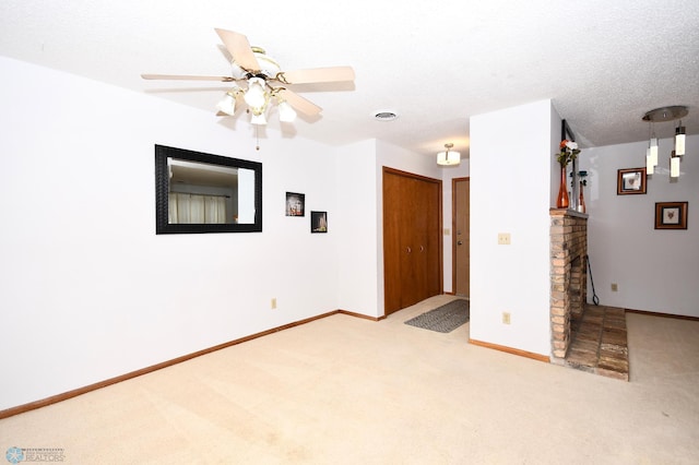 empty room with light carpet, a fireplace, ceiling fan, and a textured ceiling