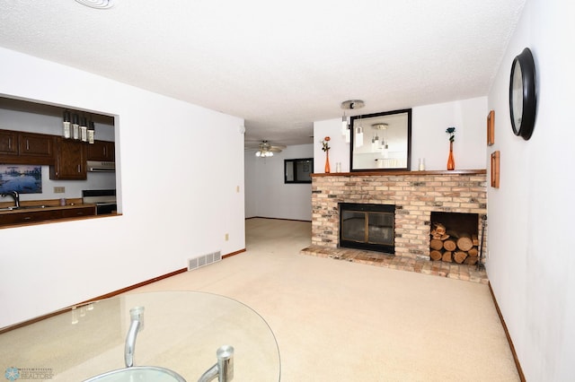 carpeted living room featuring ceiling fan, a fireplace, a textured ceiling, and sink