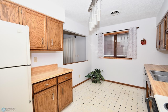 kitchen featuring a textured ceiling, white refrigerator, and sink