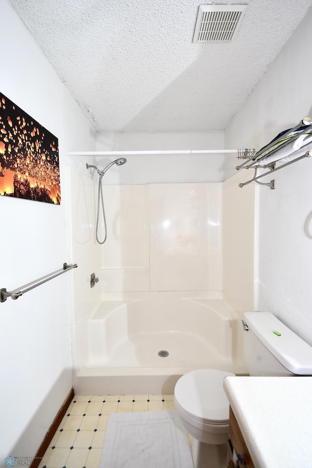 bathroom featuring tile patterned floors, a textured ceiling, a shower, toilet, and baseboards