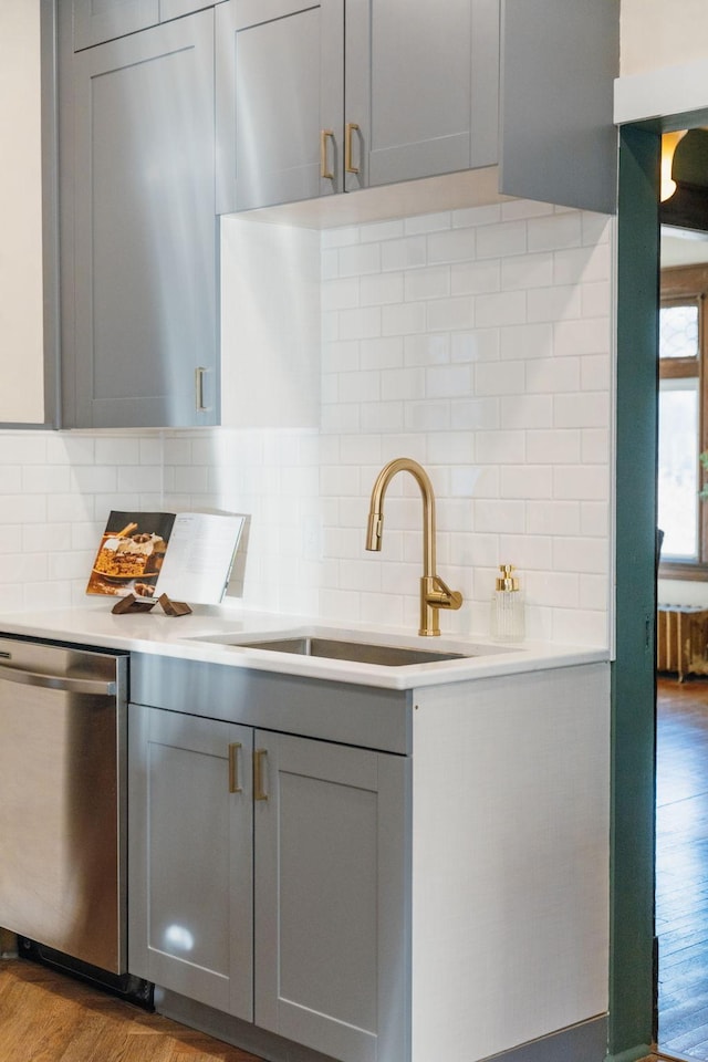 kitchen featuring light wood-type flooring, tasteful backsplash, stainless steel dishwasher, and sink