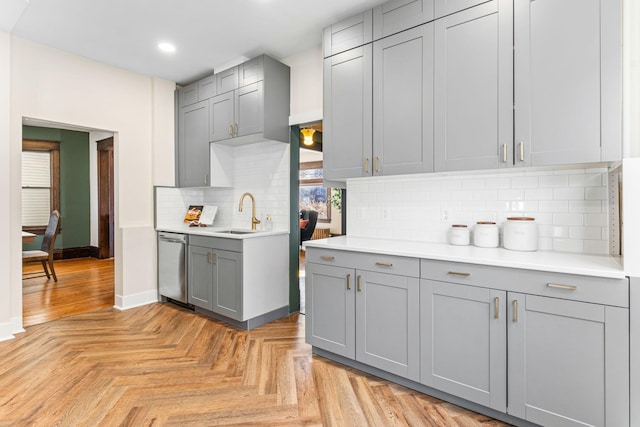 kitchen with dishwasher, light parquet floors, gray cabinetry, and sink