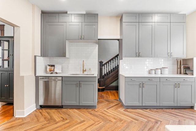 kitchen with sink, stainless steel dishwasher, backsplash, light parquet floors, and gray cabinets