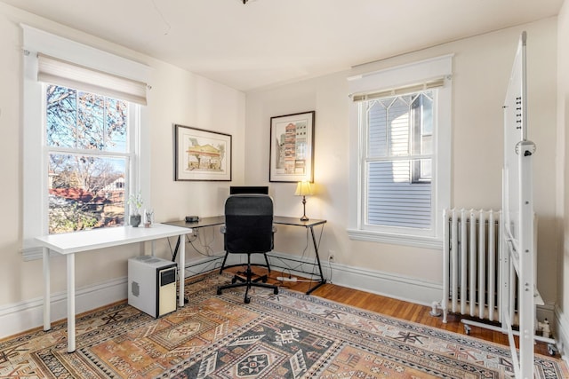 office featuring a healthy amount of sunlight, wood-type flooring, and radiator heating unit