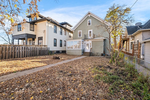 back of house featuring entry steps, a sunroom, a balcony, and fence