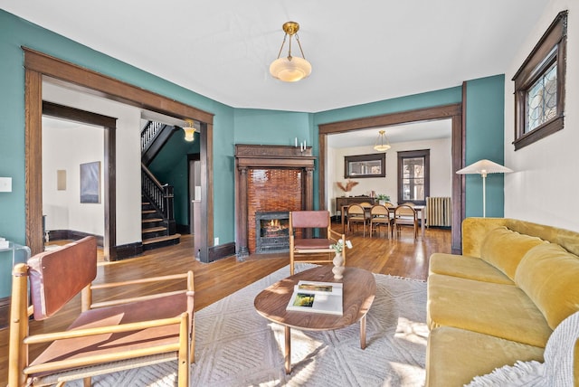 living room featuring stairs, a warm lit fireplace, wood finished floors, and radiator