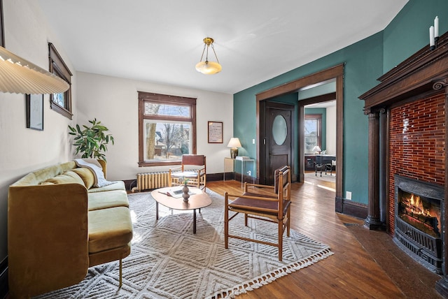 living area featuring a warm lit fireplace, hardwood / wood-style floors, baseboards, and radiator