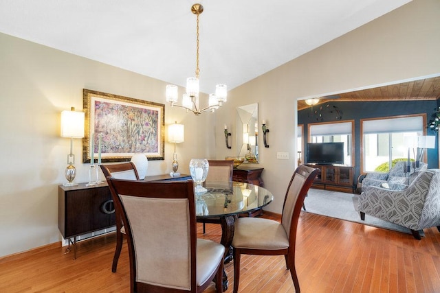 dining space with light wood-type flooring, an inviting chandelier, and vaulted ceiling