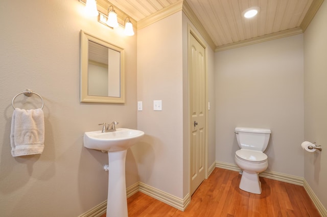 half bathroom with baseboards, toilet, wood finished floors, crown molding, and a sink