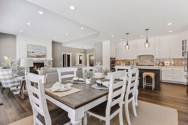 dining space with a textured ceiling, a stone fireplace, and dark hardwood / wood-style floors