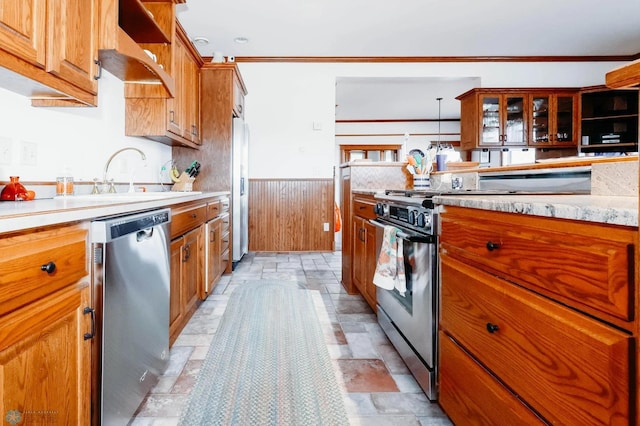 kitchen with wood walls, sink, crown molding, hanging light fixtures, and stainless steel appliances