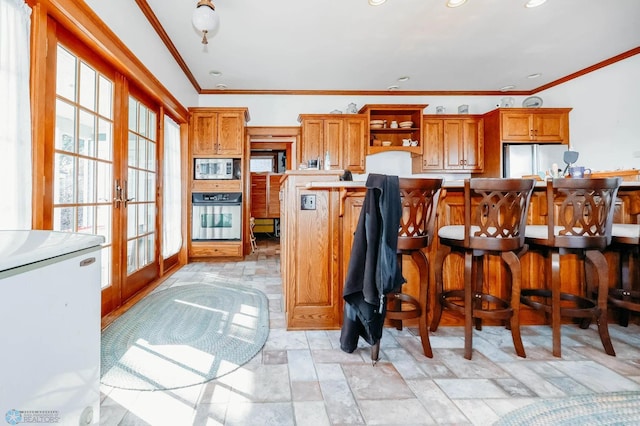 kitchen with french doors, ornamental molding, white appliances, a kitchen island, and a breakfast bar area