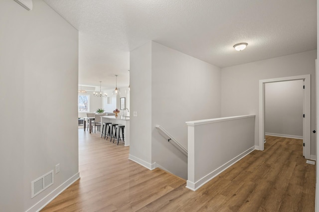 hall with hardwood / wood-style floors, a textured ceiling, and an inviting chandelier