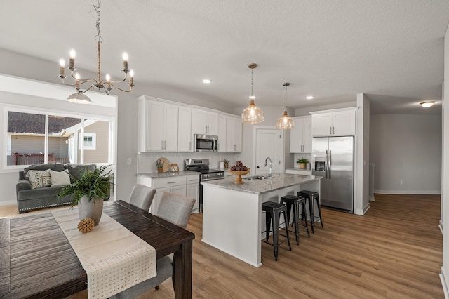 kitchen with white cabinetry, stainless steel appliances, a kitchen island with sink, a breakfast bar, and light wood-type flooring