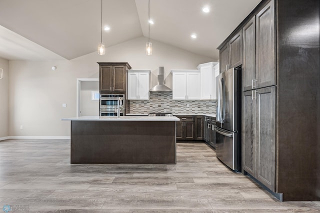 kitchen with wall chimney range hood, light hardwood / wood-style flooring, vaulted ceiling, decorative light fixtures, and appliances with stainless steel finishes