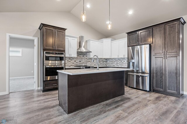 kitchen with wall chimney exhaust hood, stainless steel appliances, pendant lighting, lofted ceiling, and white cabinets