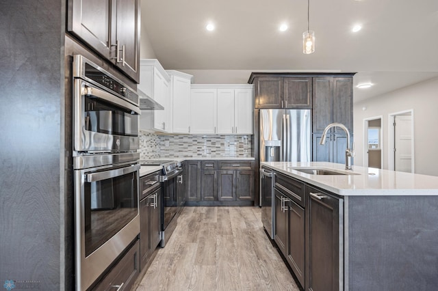 kitchen featuring white cabinets, a center island with sink, sink, light wood-type flooring, and appliances with stainless steel finishes