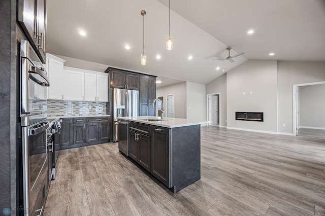 kitchen with white cabinetry, stainless steel appliances, hanging light fixtures, light hardwood / wood-style floors, and a kitchen island with sink