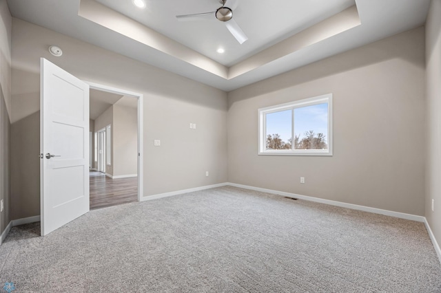 carpeted spare room with a raised ceiling and ceiling fan