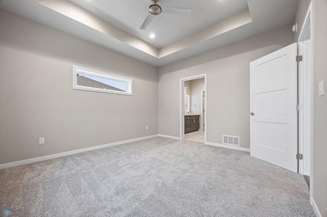 unfurnished bedroom featuring light carpet, a tray ceiling, ensuite bath, and ceiling fan