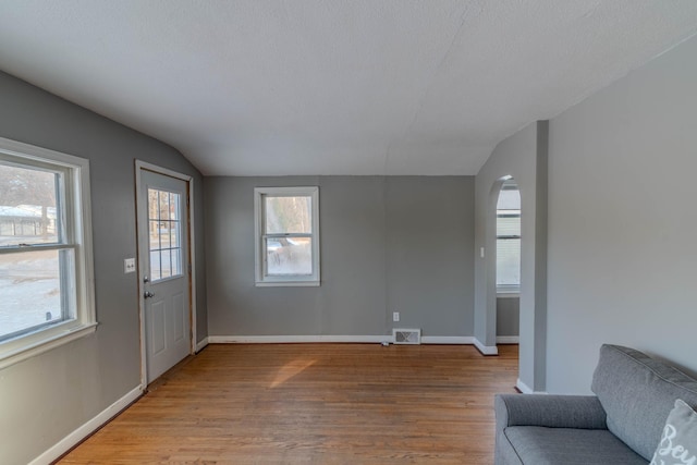 interior space featuring a textured ceiling, light wood-type flooring, and vaulted ceiling