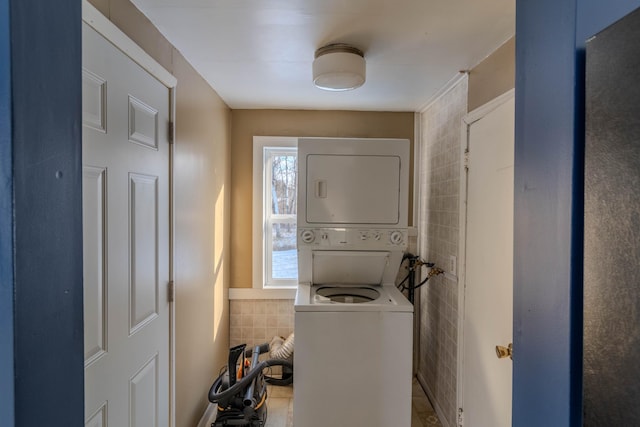 washroom with stacked washer / drying machine and tile walls