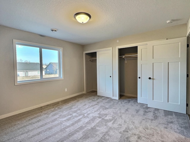 unfurnished bedroom featuring a textured ceiling, light carpet, and two closets