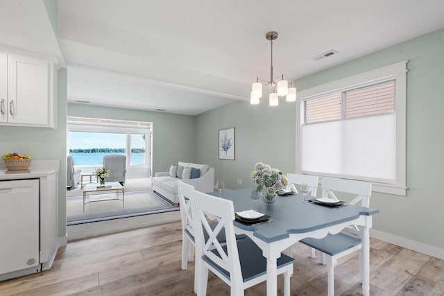 dining space featuring light hardwood / wood-style floors, a water view, and an inviting chandelier