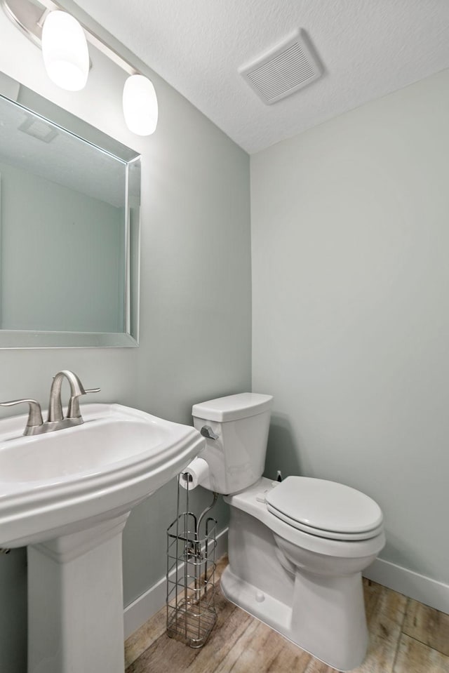 bathroom with wood-type flooring, a textured ceiling, toilet, and sink