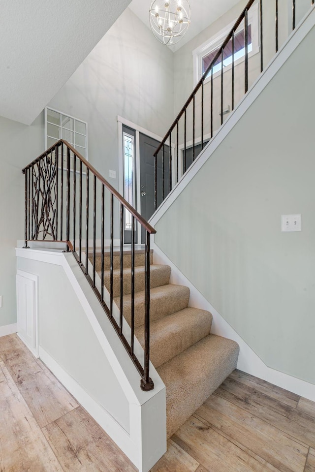 stairway with a notable chandelier, wood-type flooring, and a high ceiling