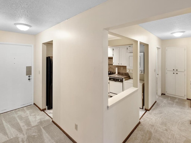 hallway featuring a textured ceiling, stacked washer / dryer, and light carpet