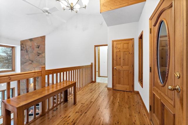 hallway with high vaulted ceiling, an inviting chandelier, and light hardwood / wood-style flooring