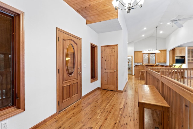 foyer with baseboards, light wood-type flooring, ceiling fan with notable chandelier, arched walkways, and high vaulted ceiling