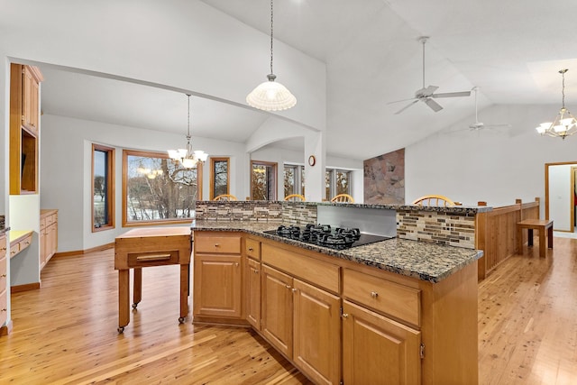 kitchen featuring pendant lighting, light hardwood / wood-style flooring, dark stone countertops, backsplash, and black gas stovetop