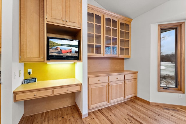 kitchen featuring light brown cabinetry, built in desk, vaulted ceiling, and light hardwood / wood-style floors