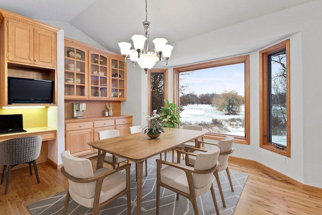 dining area with baseboards, vaulted ceiling, light wood-style flooring, a notable chandelier, and built in study area