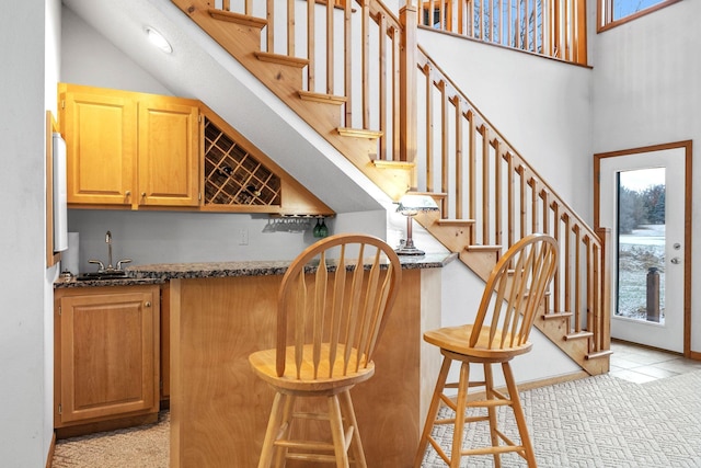 bar featuring stairway, indoor wet bar, light tile patterned floors, a towering ceiling, and a sink