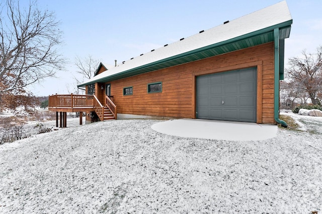 snow covered house featuring a wooden deck and a garage